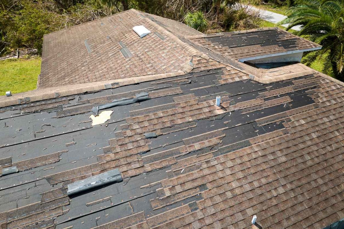 Damaged house roof with missing shingles after hurricane Ian in Florida. Consequences of natural disaster.